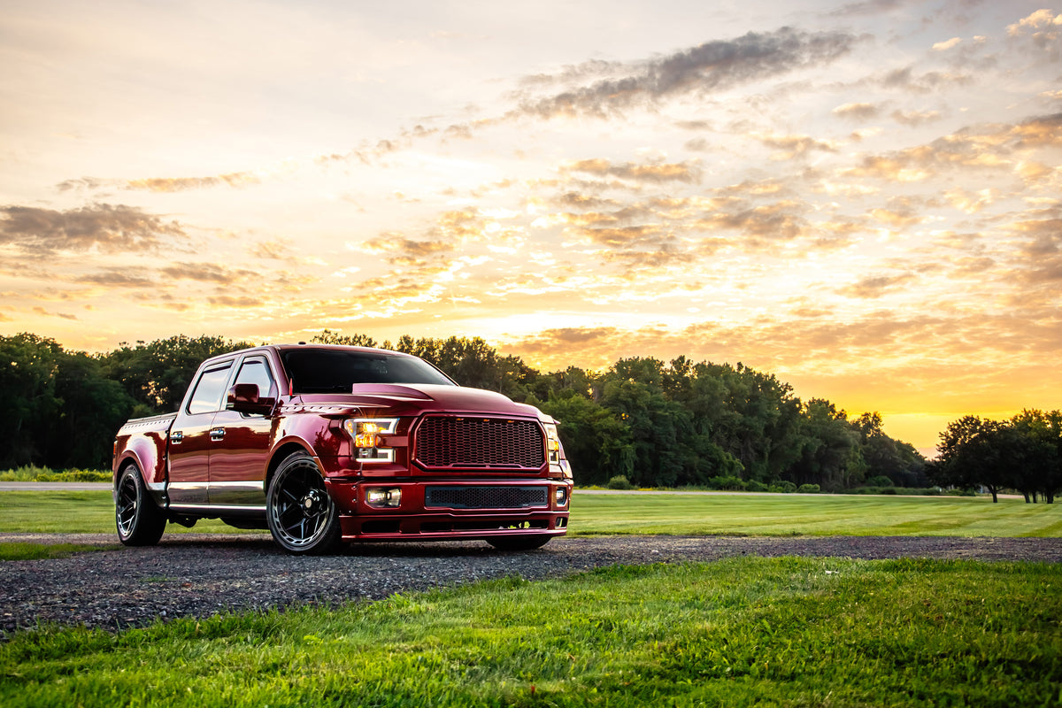 Clinched widebody kit on 2015-2017 Ford F-150 Crew Cab, red and grey, front three-quarter view on grass at sunset