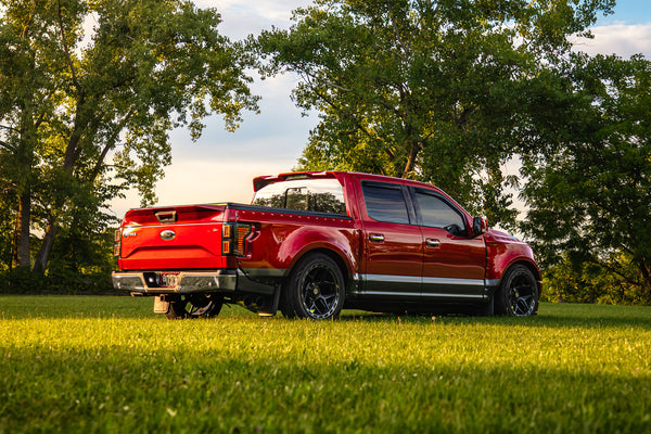 Clinched widebody kit on 2015-2017 Ford F-150, red and grey, low rear three-quarter view in a field